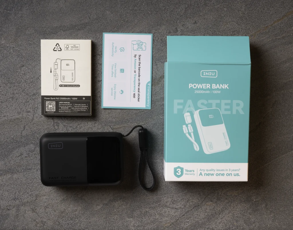 The contents of the box from top left: manual, warranty card, the box, and the power bank with USB-C cord in the lanyard clip.