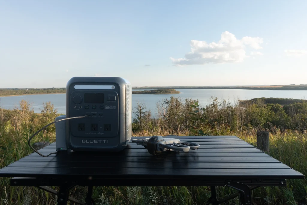 A BLUETTI Elite 100 mini on a table charging a drone.  There is a lake in the background.